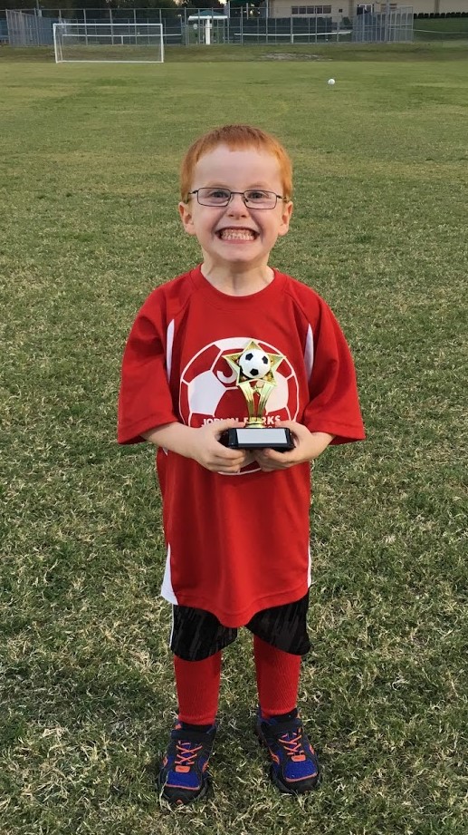 Jameson posing on the soccer field with a trophy